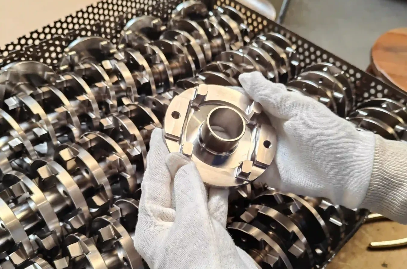 Pièce métallique manipulée avec des gants au-dessus d’un ensemble de composants industriels