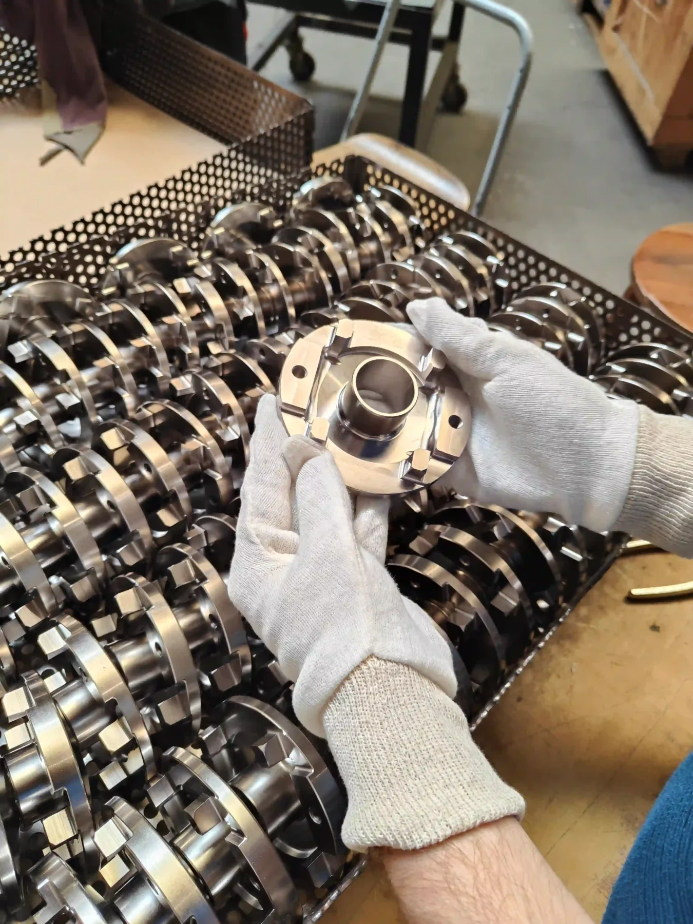 Manipulation d’une pièce métallique en atelier Pièce métallique manipulée avec des gants au-dessus d’un ensemble de composants industriels